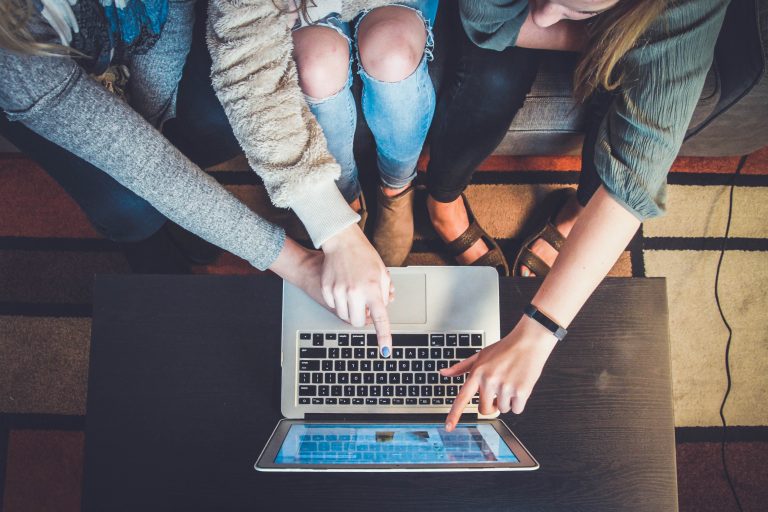 four hands pointing at a macbook screen