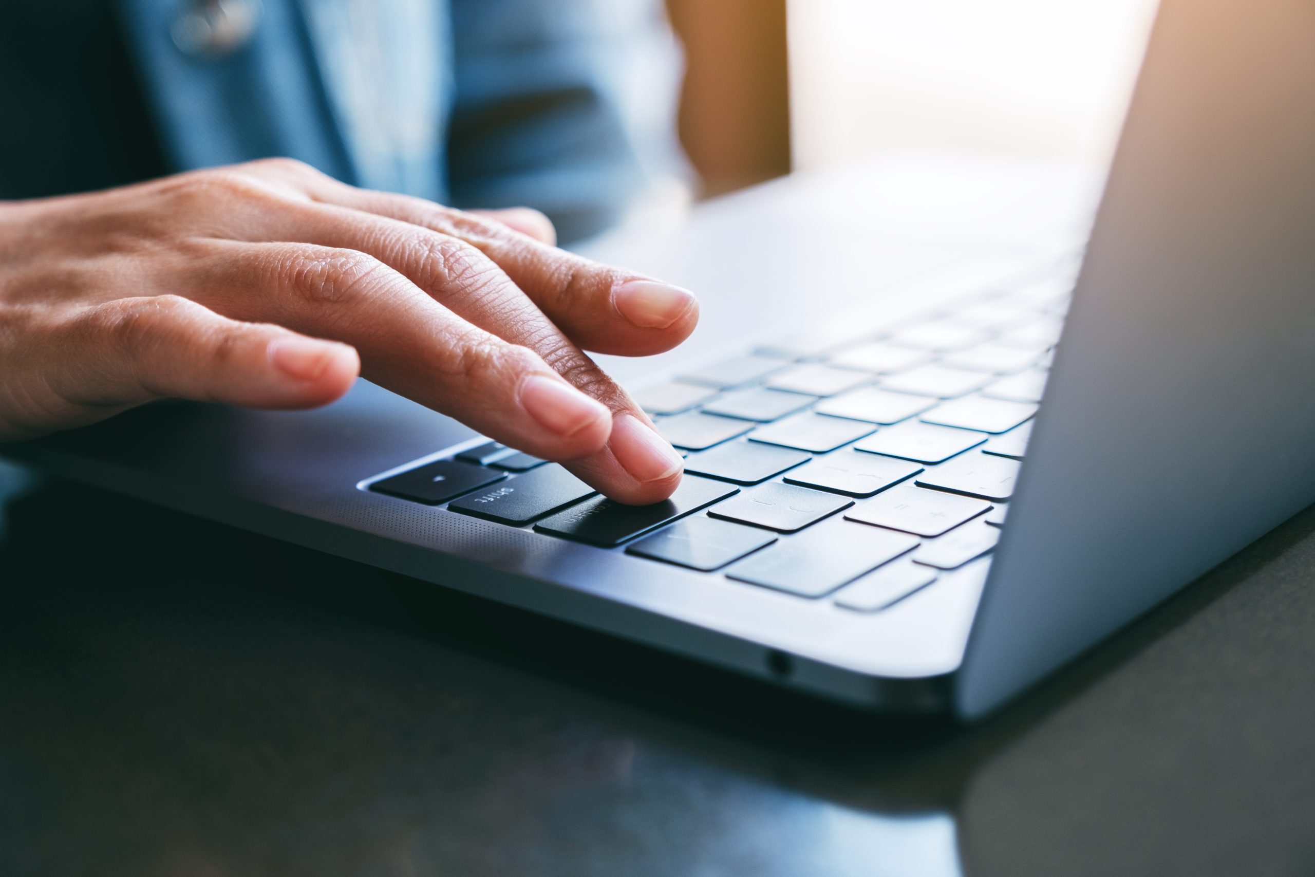 Closeup image of a woman's finger pressing on the enter button of laptop computer on the table